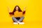 Young smiling confused woman sitting on floor with laptop isolated on yellow background