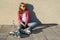 Young smiling cool girl shod in rollerblades, sits on the sidewalk and holding a water bottle.