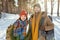 Young smiling couple in winterwear standing in front of camera in the forest