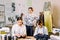 Young smiling fashion designer posing with handmade pants on hangers at sewing atelier and looking at camera. Two pretty