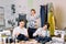 Young smiling fashion designer posing with handmade pants on hangers at sewing atelier and looking at camera. Two pretty