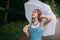 Young smiling girl with blond long hair, in a blue summer dress and blue beads, stands with a white umbrella