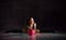 Young smiling girl gymnast in black sport body and uppers sitting in twine on floor and holding pink gymnastic ball in hands