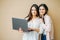 Young smiling girls students in casual with laptop in hands  on beige background