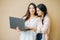 Young smiling girls students in casual with laptop in hands  on beige background