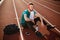 Young smiling guy in red headphones happily looking aside with towel on shoulder on running track of stadium