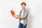 Young smiling handsome man in protective orange hardhat holding opened case with instruments or toolbox isolated on