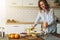 Young smiling housewife standing in kitchen near table is cooking dinner, cleaning dishes. Girl is making breakfast