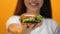 Young smiling lady proposing yummy hamburger, fast food restaurant, close up