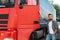 Young smiling male truck driver beside his red cargo truck