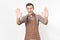 Young smiling man chef or waiter in striped brown apron, shirt showing palms to camera isolated on white background