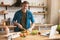 Young smiling man cutting tomatoes with knife while cooking breakfast in the kitchen checking recipe in his laptop , sunday