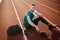 Young smiling man joyfully looking in camera with white towel on shoulder while spending time on running track of