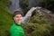 Young smiling man with waterfall and green canyon on background takes a Selfie. Concept of freedom movement and freedom