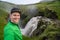 Young smiling man with waterfall and green canyon on background takes a Selfie. Concept of freedom movement and freedom