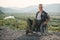 Young smiling man in wheelchair enjoying nature beauty on the mountains. People with disabilities travelling.