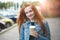 Young smiling red hair woman holding paper coffee cup, enjoying coffee, having fun