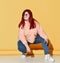 Young smiling red haired overweight woman in casual clothing and sunglasses sits squatting and looking aside