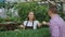 Young smiling seller florist working in garden center. Woman gives shopping bag to customer and making payment by credit