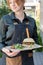 A young smiling waitress with freckles is holding a burger with meat. Service in the restaurant concept.