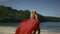 Young smiling woman with blonde hair in elegant long red dress walking on beach