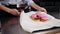 Young smiling woman in blue shirt and black apron on a final stage of preparing french dessert - putting pink glazed