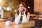 Young smiling woman having pleasant phone talk working outside office during lunch break drinking hot coffee in trendy cafe