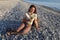 Young smiling woman hiker sits on deserted pebble beach and holds small bouquet of wildflowers