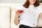 Young smiling woman holding cocktail glass in hand with red alcohol drink sitting on sofa at home