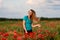 Young smiling woman with long hair standing on field with red poppies.