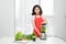 Young smiling woman making smoothie with fresh greens in the blender in kitchen at home. Healthy vegetarian smoothie for weight l