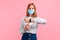 Young smiling woman in a medical mask, looking at the clock on her hand, on a pink background