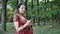 Young smiling woman in red Sari Indian ethnic prints SMS message on phone in summer Park