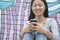 Young smiling woman sitting against a wall with graffiti and looking down and texting on her phone