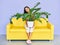 Young smiling woman sitting on sofa holding huge plant in pot