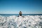 Young smiling woman sitting on a top of frozen sea ice blocks on a coast of the sea with a blue sky at the background