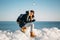 Young smiling woman sitting on the top of sea ice blocks on the coast holding broken piece of ice with a blue sea and