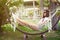 Young smiling woman in sunglasses resting in hammock in backyard