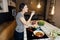 Young smiling woman tasting a healthy keto meal in home kitchen.Making dinner on kitchen island standing by induction hob.