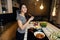 Young smiling woman tasting a healthy keto meal in home kitchen.Making dinner on kitchen island standing by induction hob.