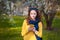 Young smilling woman standing in a blooming garden and writes on mobile phone. Blooming cherry. Portrait of beautiful woman