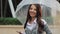 Young smilling woman stands with umbrella in her hand on the street and looking into the camera.. She holds the