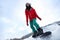 Young snowboarder wearing Santa hat on snowy hill, low angle view. Winter vacation