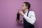 Young sommelier guy checks the smell of red wine on a colored background, an expert on wine in a white shirt and apron holds a