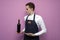 Young sommelier guy holds a bottle of red wine on a colored background, an expert on wine in a white shirt and apron, the waiter