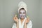 Young spa woman in face mask smiling and holding green cucumber. Female model in blue moisturizing cosmetic mask. Facial treatment