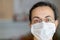 Young Spanish woman in protective sterile medical mask on her face looking at camera at home