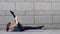 Young sport woman doing yoga and pilates fitness exercises on grey urban background and pink yoga mat