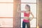 Young sportgirl is working out with dumbbells in bright warm room. Side portrait of satisfied girl, who feels healthy and full