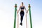 Young sportive athlete woman doing fitness exercise on metal bars outdoors at stadium court